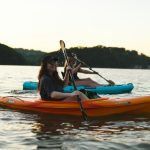 Woman in blue shirt and blue denim jeans riding orange kayak on water during daytime
